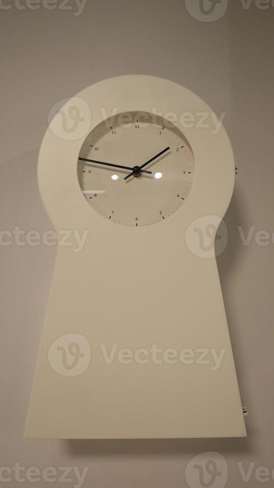 Unique white wall clock shaped like a keyhole. photo