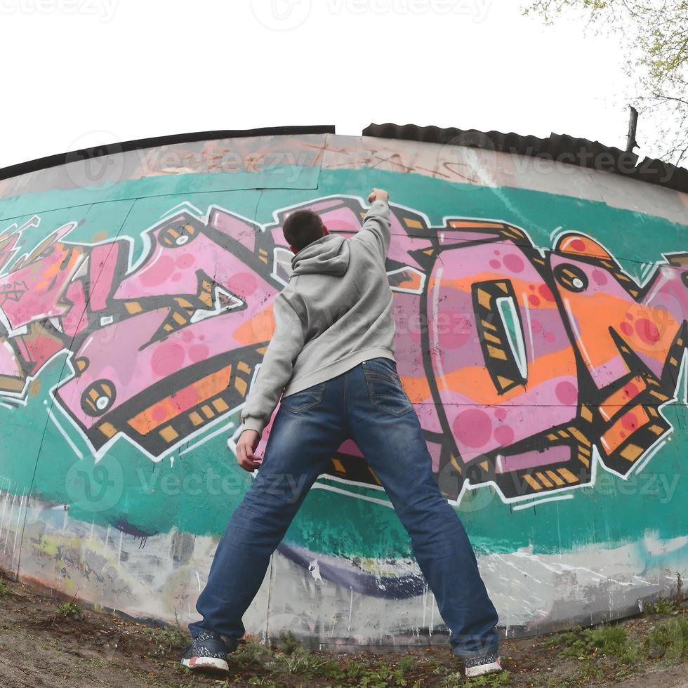 A young guy in a gray hoodie paints graffiti in pink and green c photo