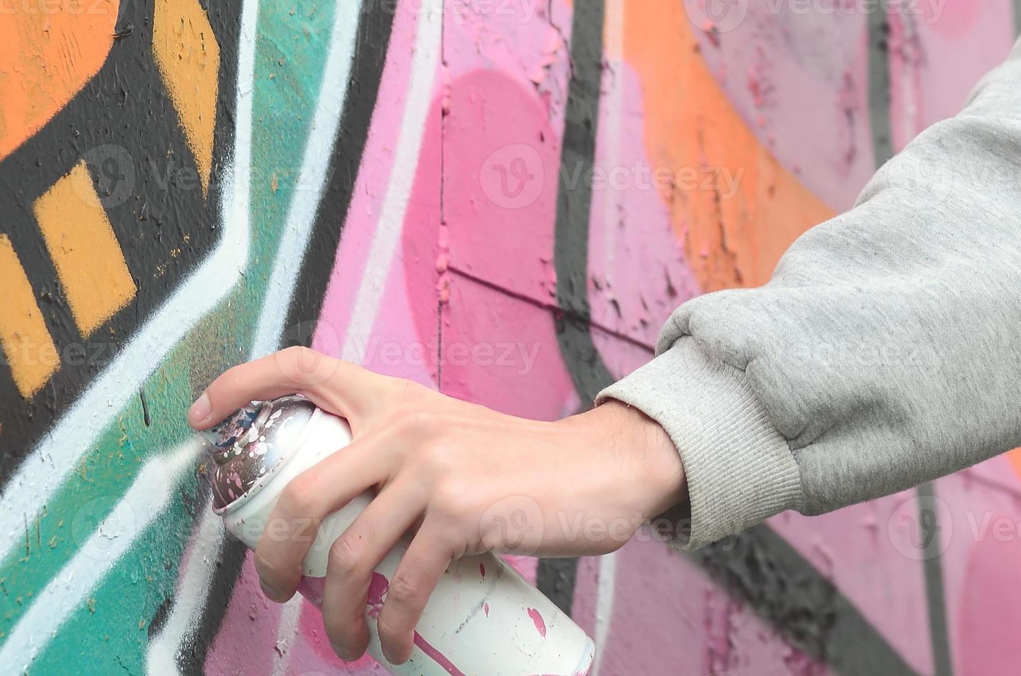 A young guy in a gray hoodie paints graffiti in pink and green c photo