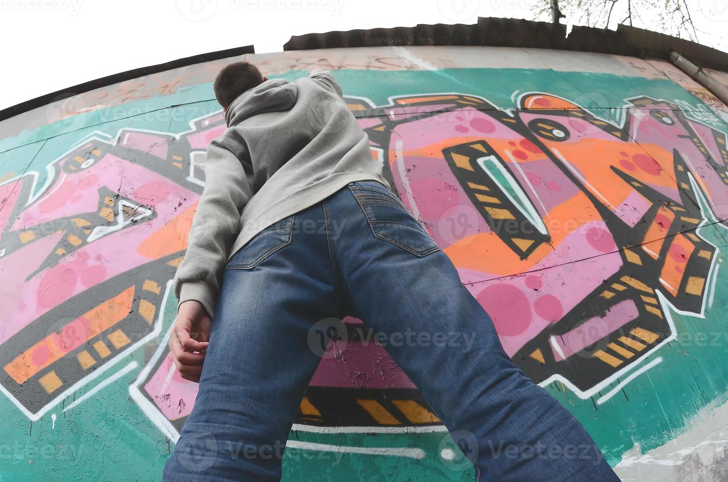 A young guy in a gray hoodie paints graffiti in pink and green c photo