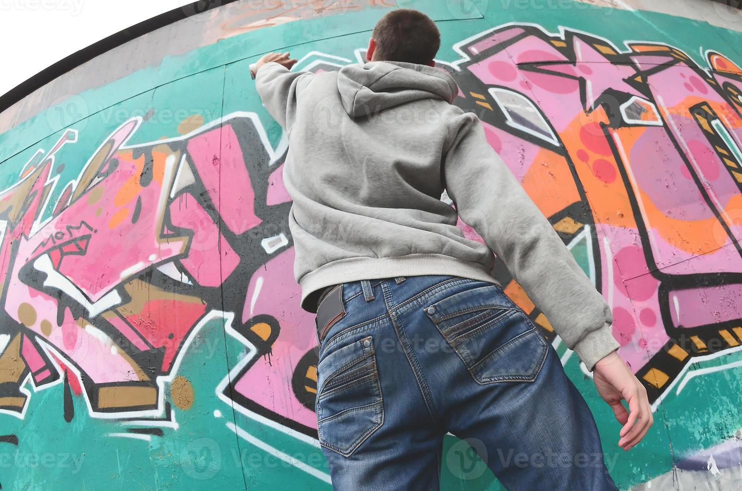 A young guy in a gray hoodie paints graffiti in pink and green c photo