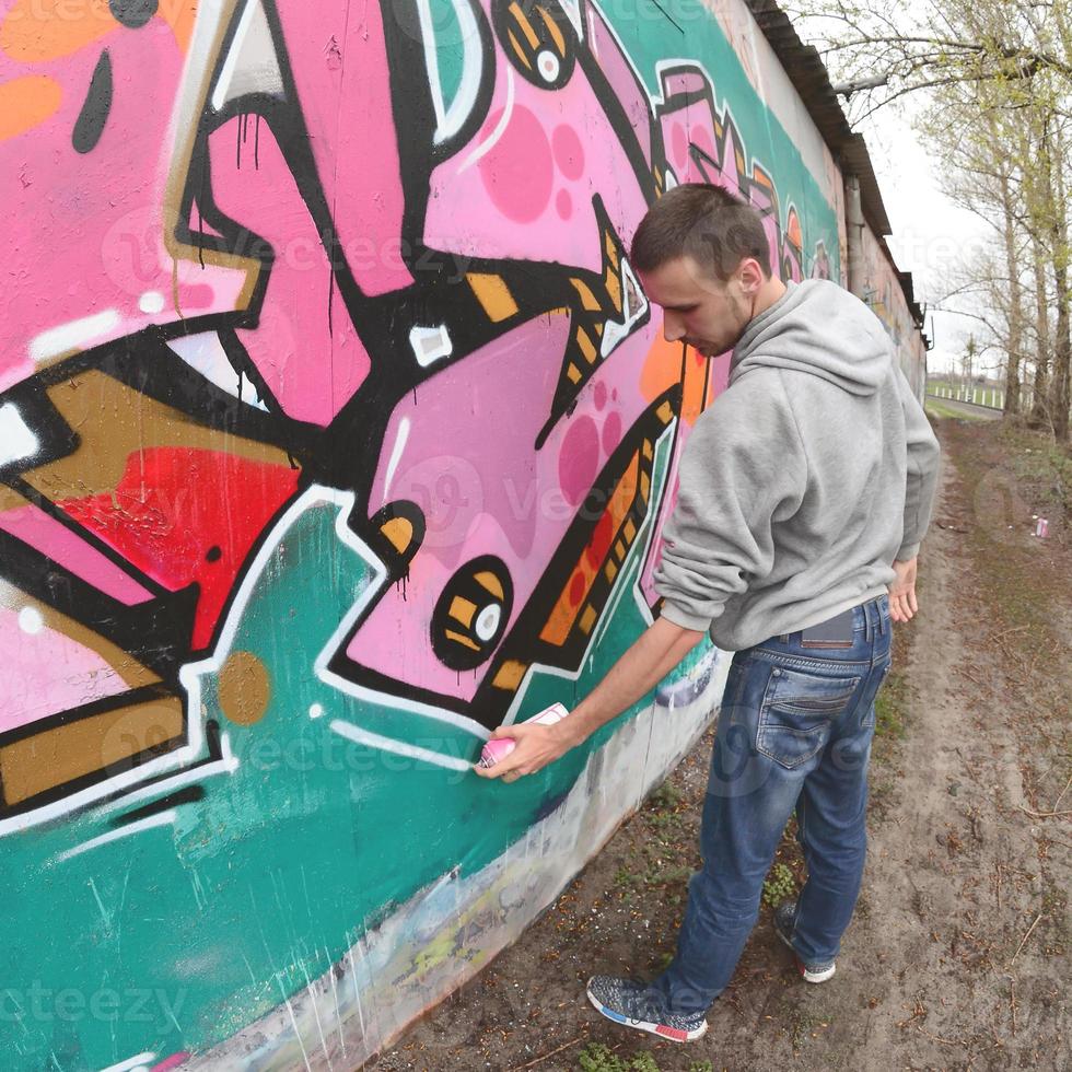 A young guy in a gray hoodie paints graffiti in pink and green c photo