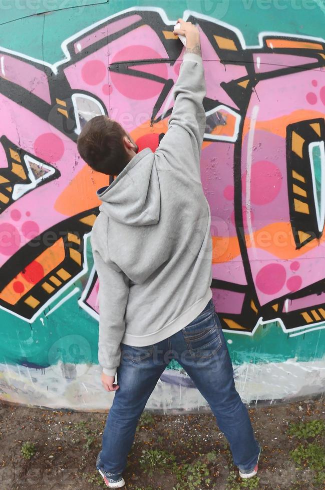 A young guy in a gray hoodie paints graffiti in pink and green c photo