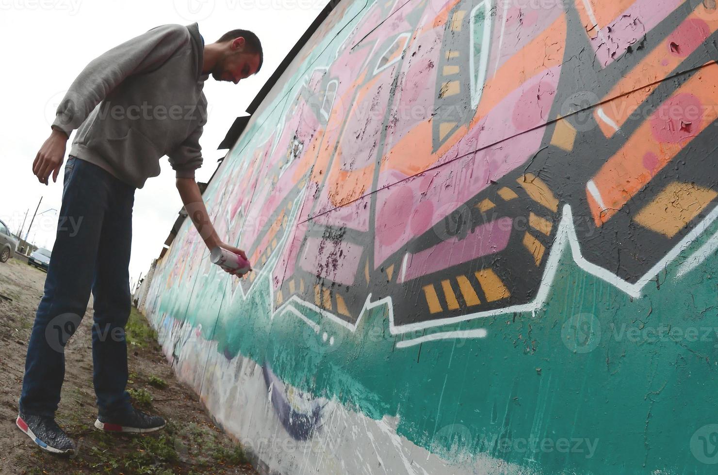 A young guy in a gray hoodie paints graffiti in pink and green c photo