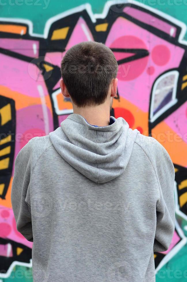 A young graffiti artist in a gray hoodie looks at the wall with photo