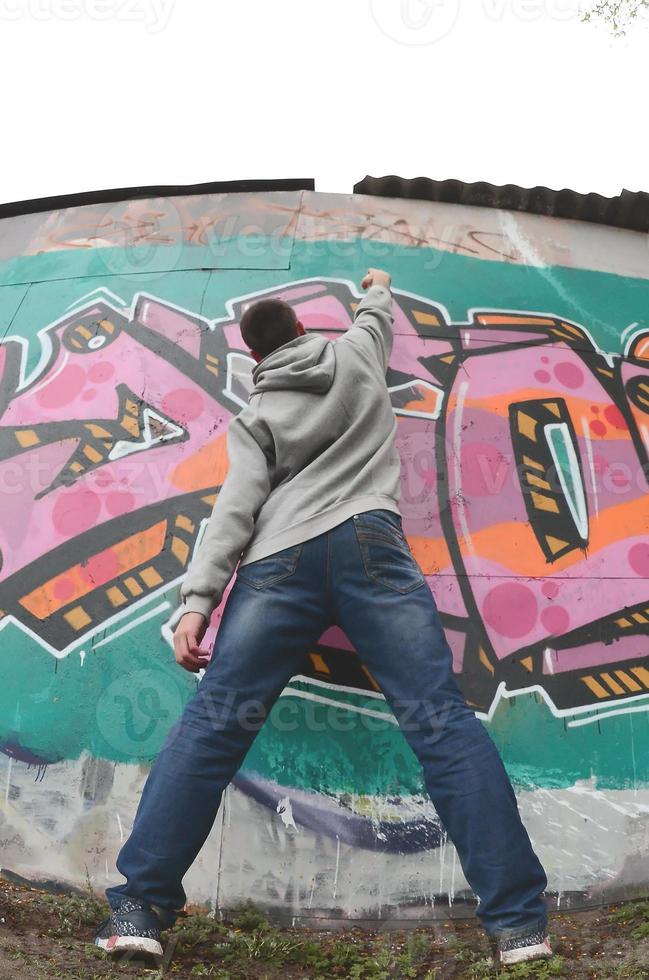 A young guy in a gray hoodie paints graffiti in pink and green c photo