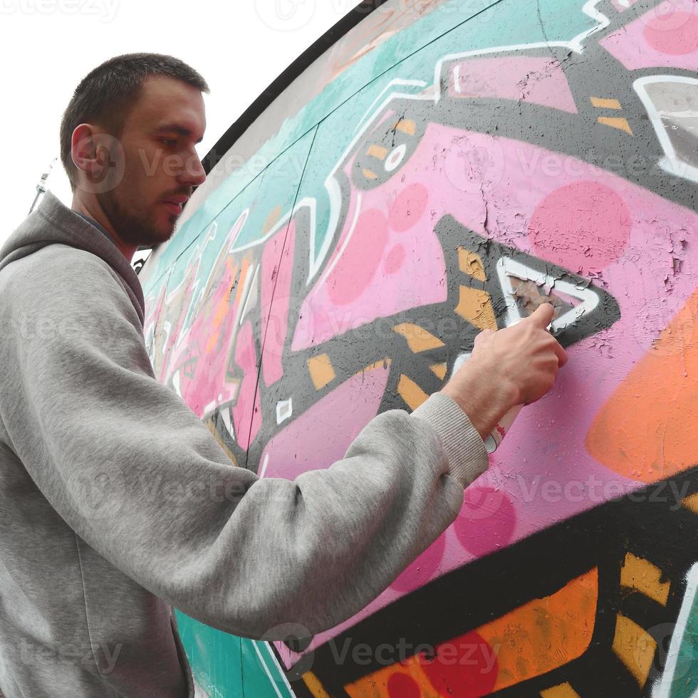 A young guy in a gray hoodie paints graffiti in pink and green c photo