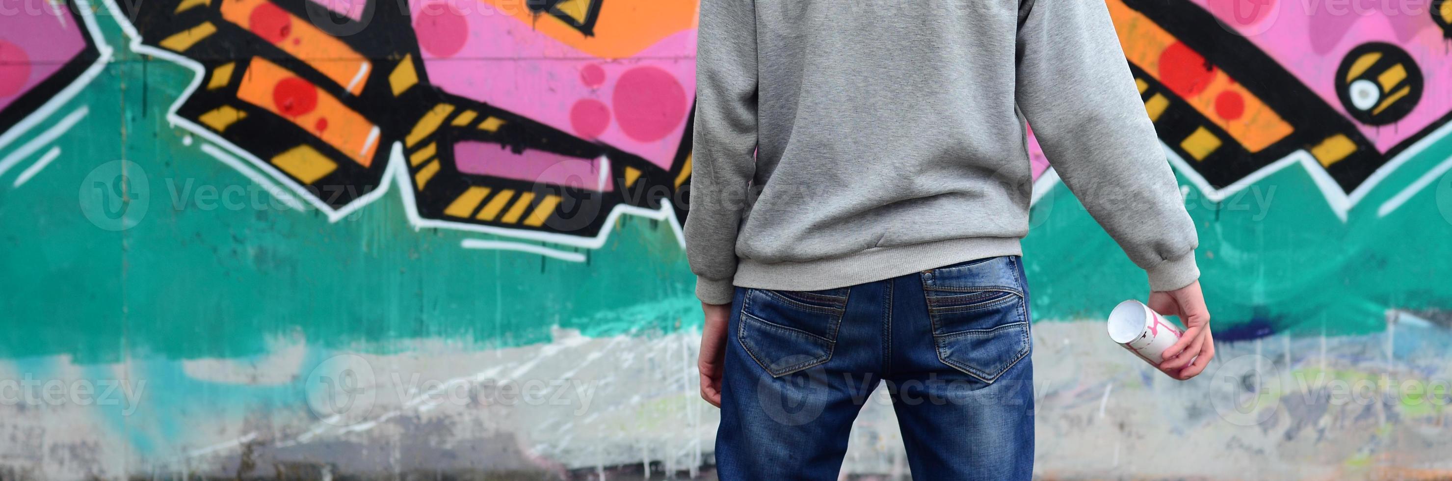 A young graffiti artist in a gray hoodie looks at the wall with photo