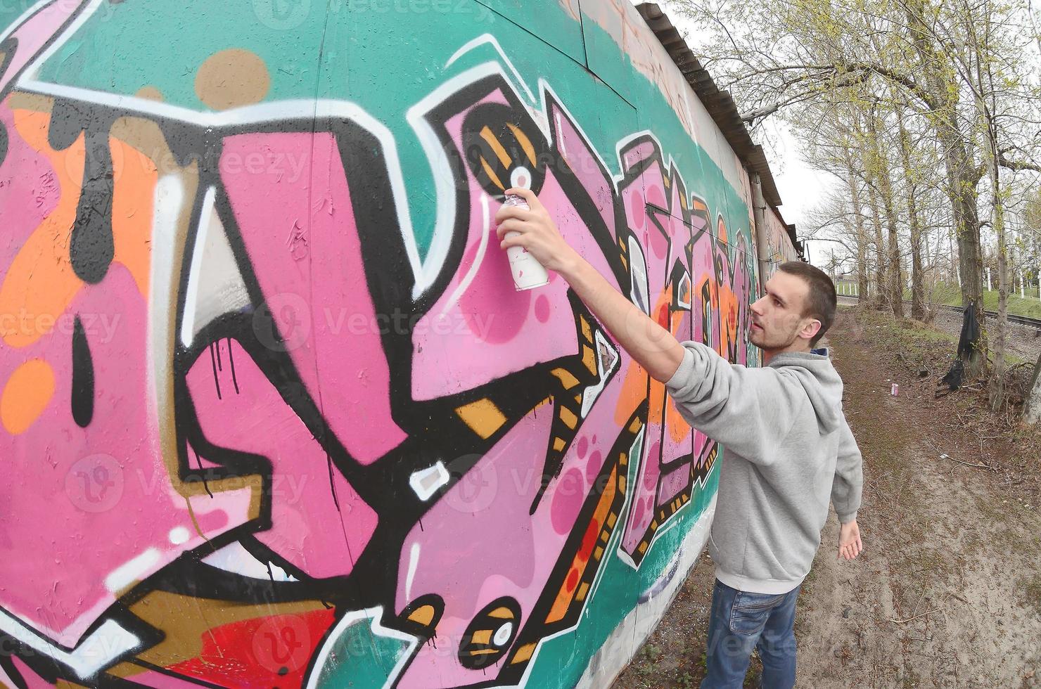 un joven con una sudadera con capucha gris pinta graffiti en rosa y verde c foto