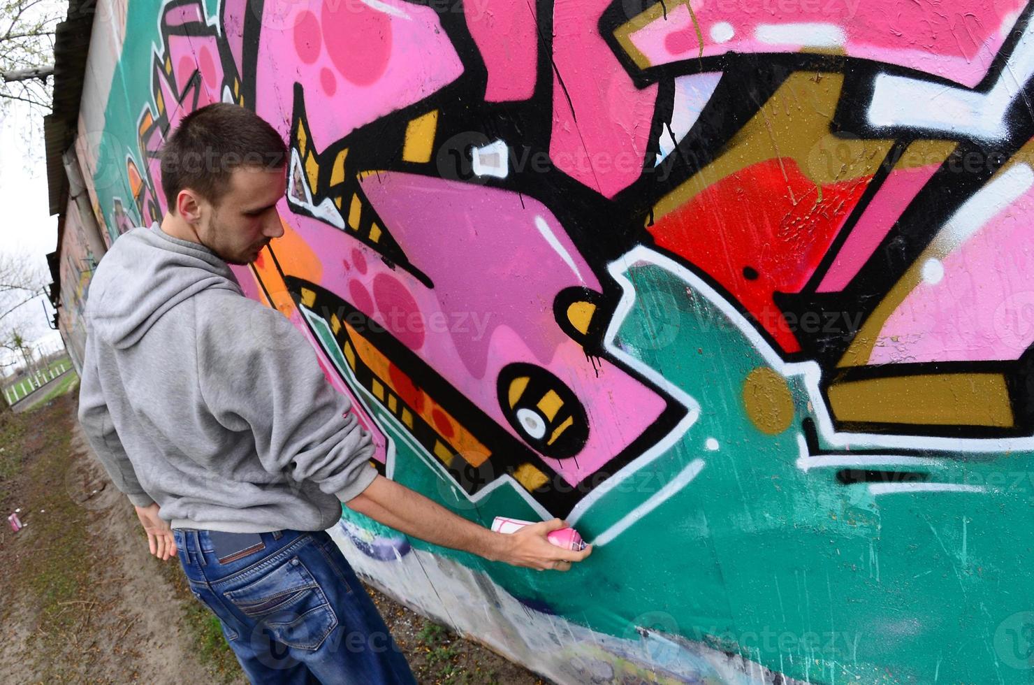 A young guy in a gray hoodie paints graffiti in pink and green c photo