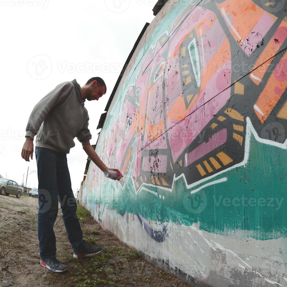 A young guy in a gray hoodie paints graffiti in pink and green c photo