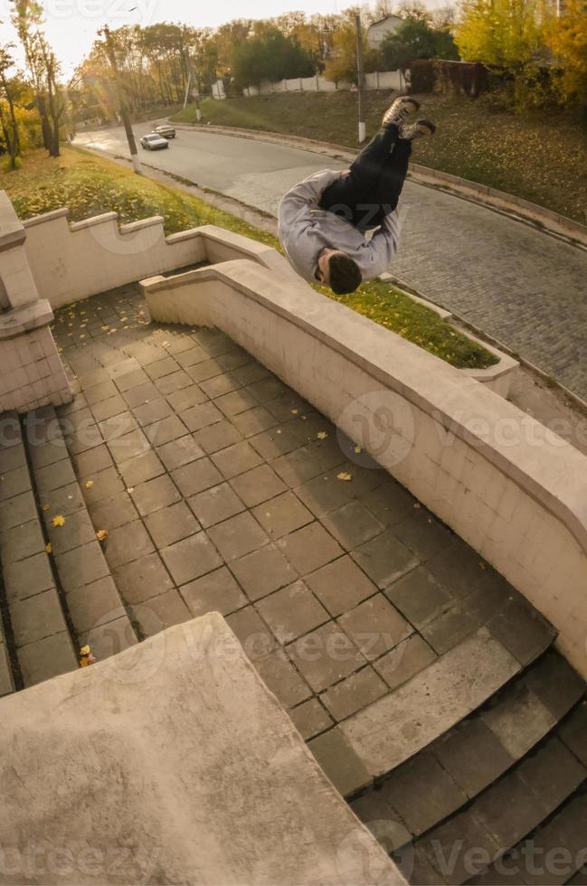 A young guy performs a side flip in the autumn park. The athlete practices parkour, training in street conditions. The concept of sports subcultures among youth photo