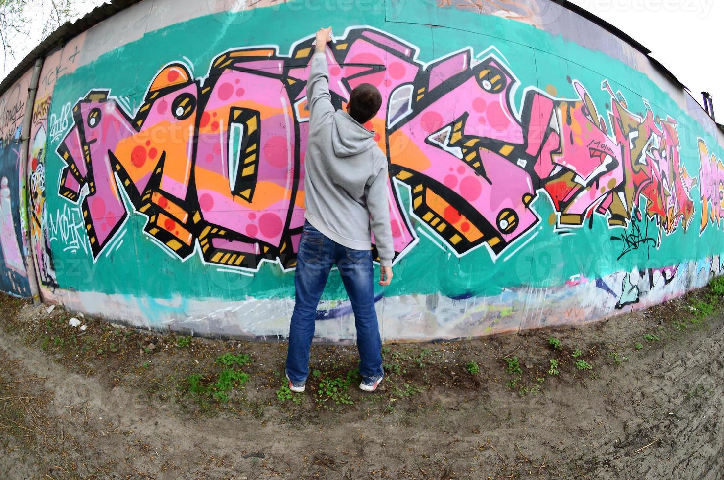 A young guy in a gray hoodie paints graffiti in pink and green c photo