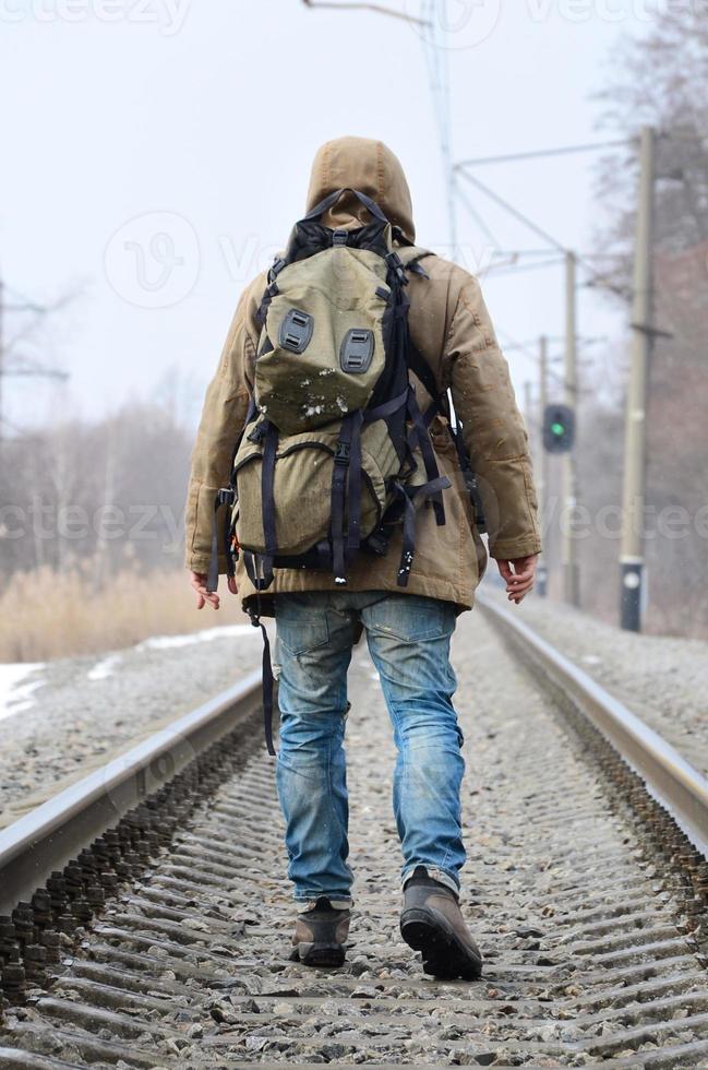 A man with a large backpack goes ahead on the railway track duri photo