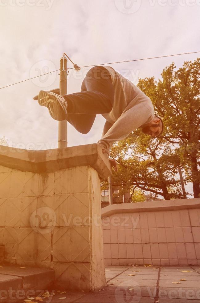 A young guy performs a jump through the concrete parapet. The athlete practices parkour, training in street conditions. The concept of sports subcultures among youth photo
