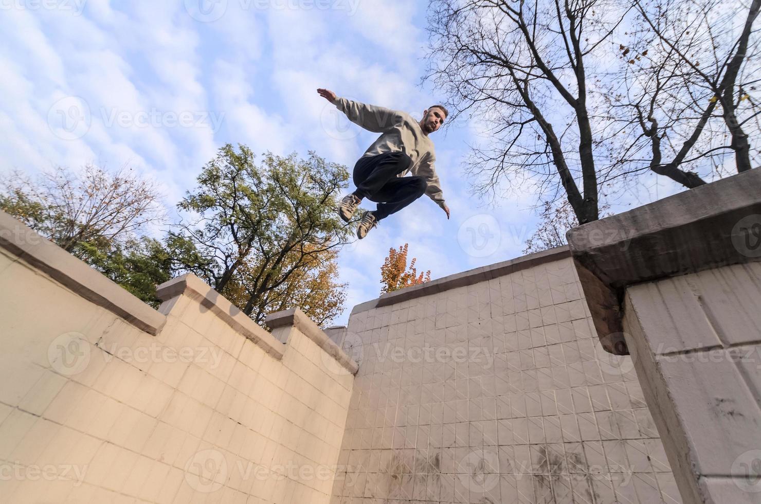 A young guy performs a jump through the space between the concrete parapets. The athlete practices parkour, training in street conditions. The concept of sports subcultures among youth photo