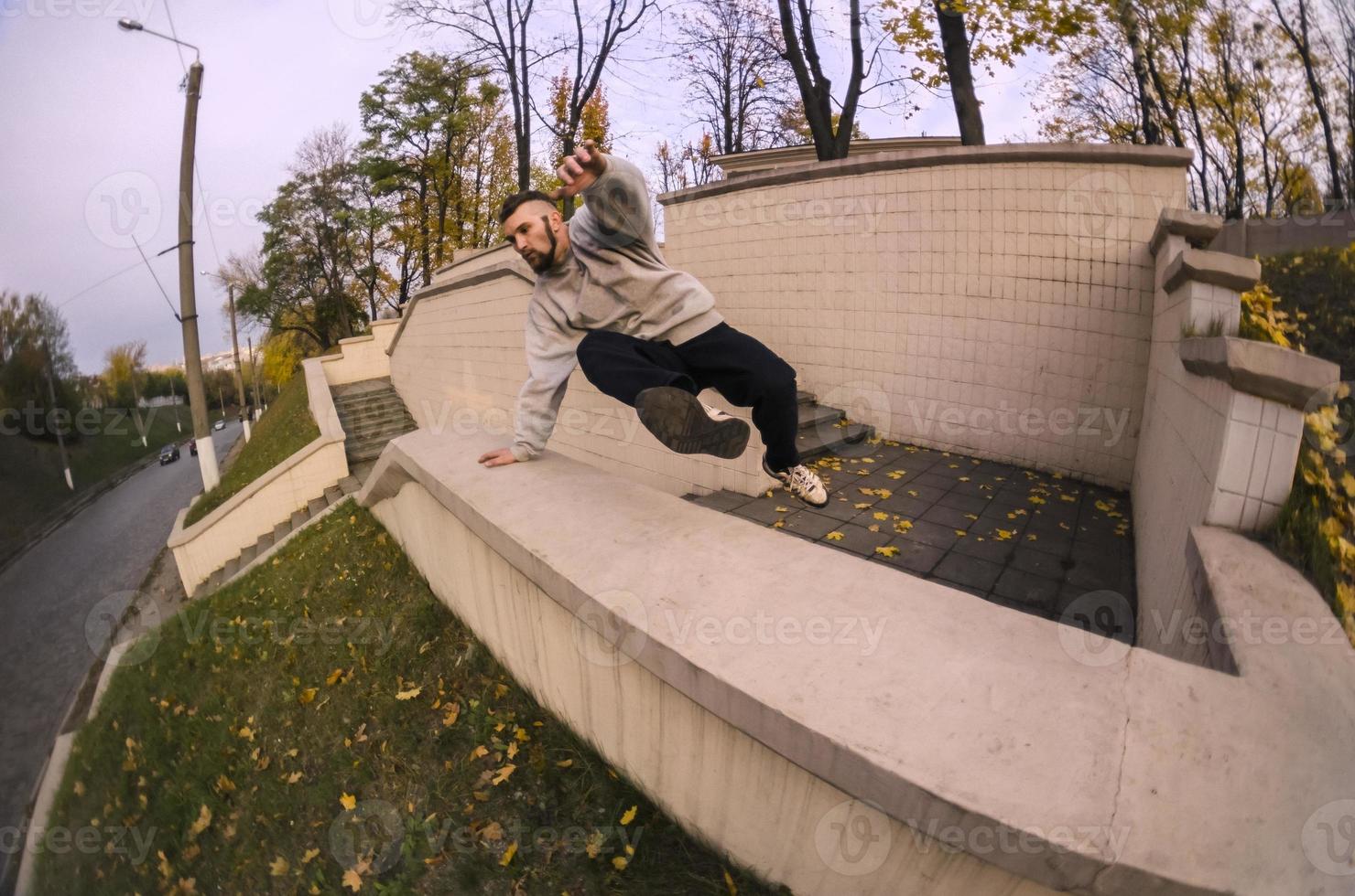 A young guy performs a jump through the concrete parapet. The athlete practices parkour, training in street conditions. The concept of sports subcultures among youth photo