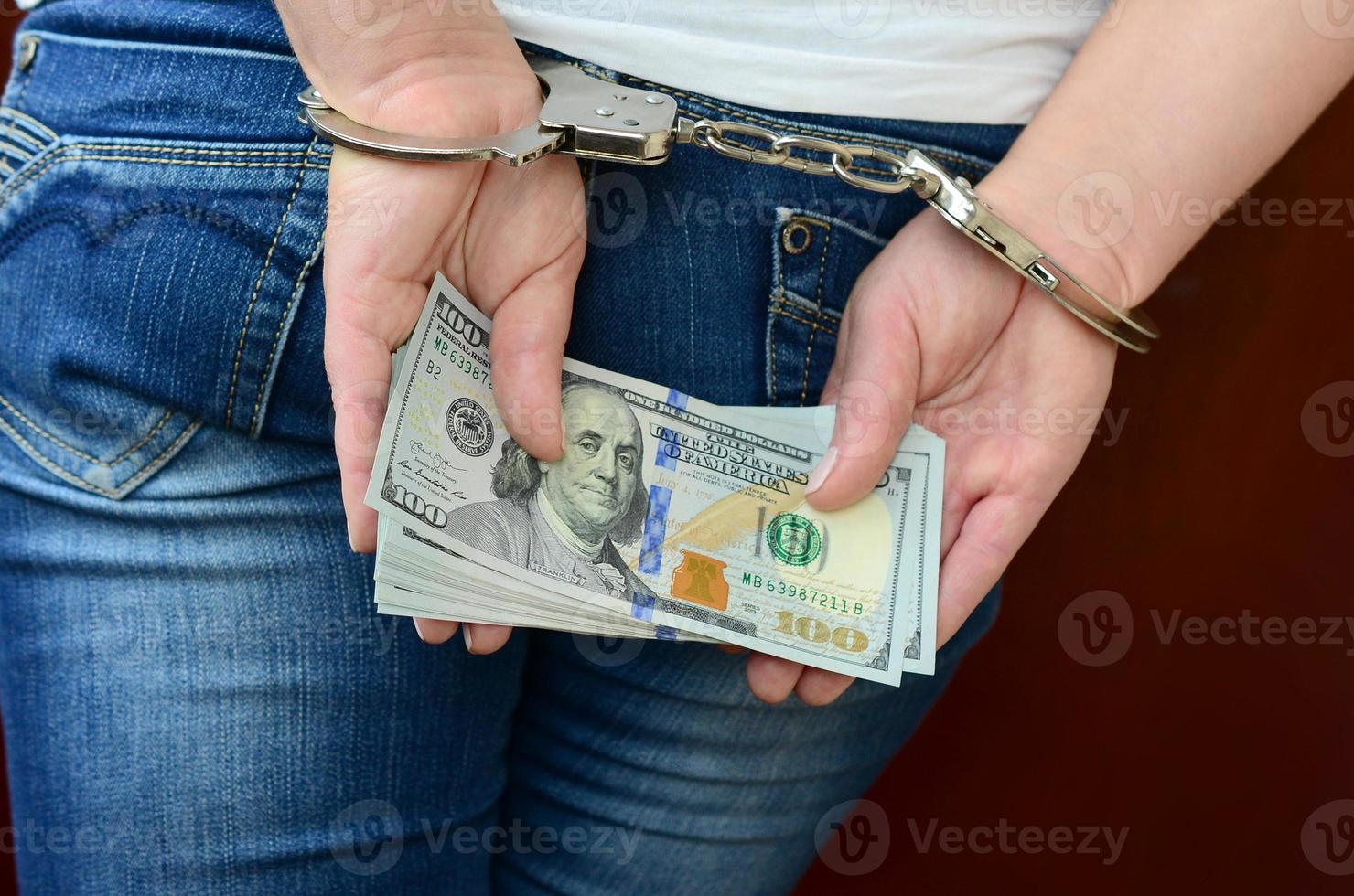 An arrested girl with handcuffed hands with a huge amount of dollar bills. Back view photo