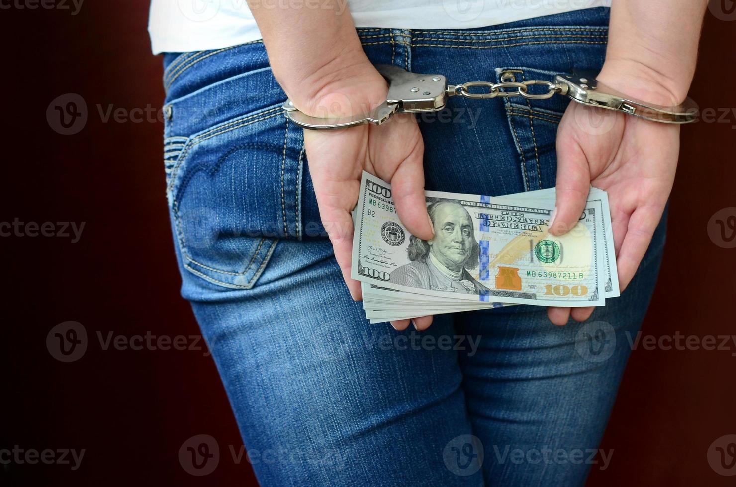 An arrested girl with handcuffed hands with a huge amount of dollar bills. Back view photo