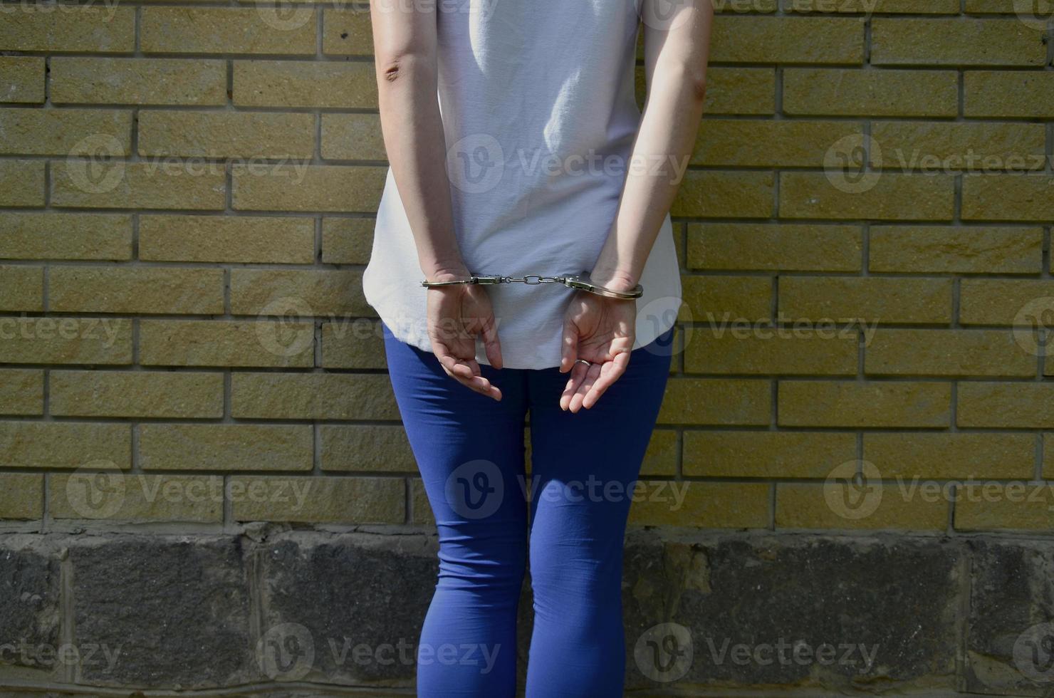 fragmento del cuerpo de una joven criminal con las manos esposadas contra un fondo de pared de ladrillo amarillo. el concepto de detener a un delincuente de una mujer criminal en un entorno urbano foto