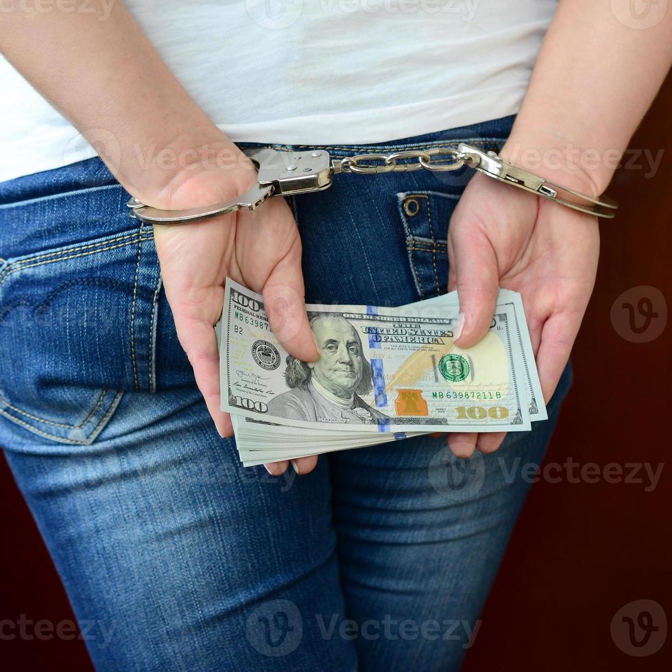 An arrested girl with handcuffed hands with a huge amount of dollar bills. Back view photo