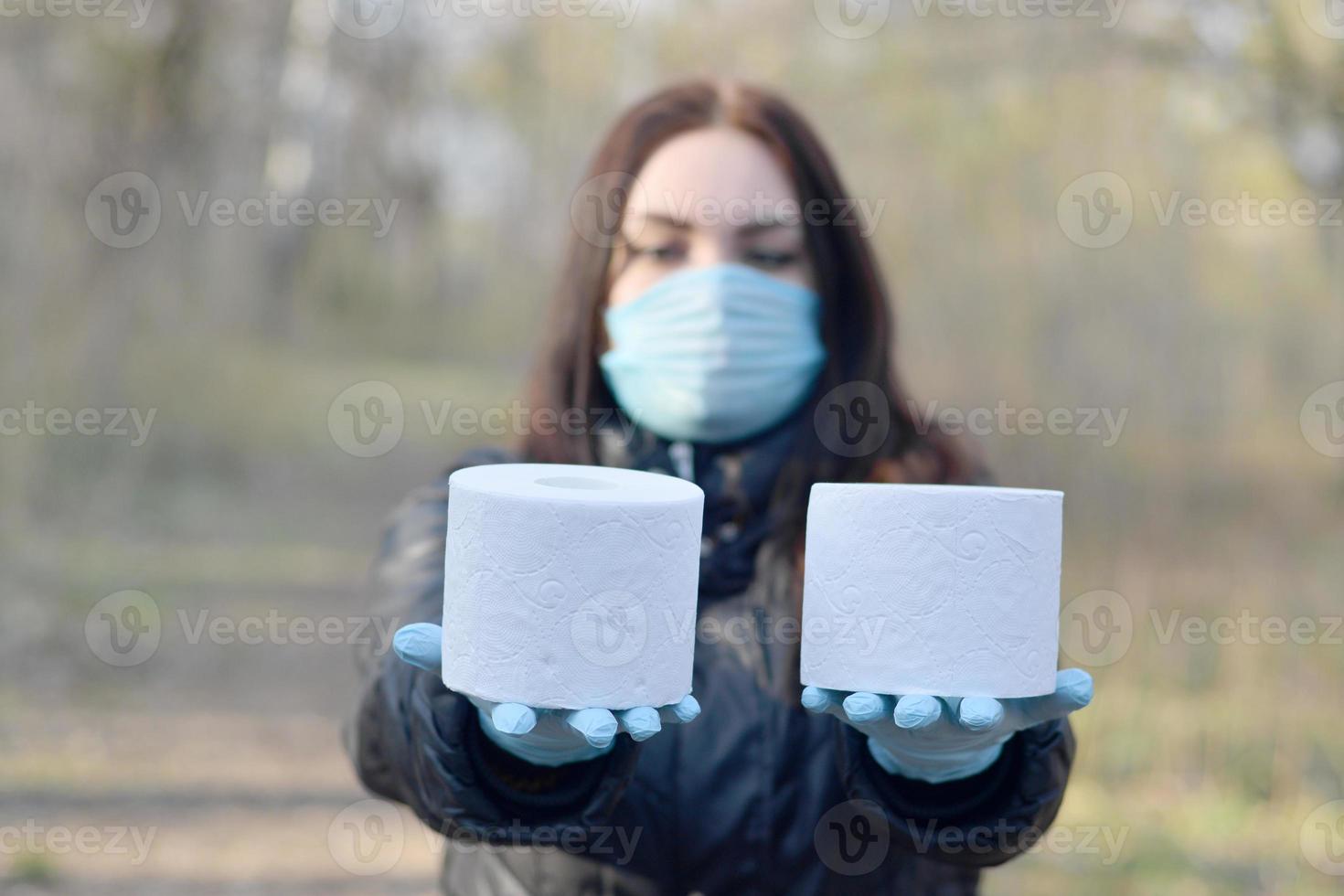 Covidiot concept. Young woman in protective mask holds many rolls of toilet paper outdoors in spring wood photo