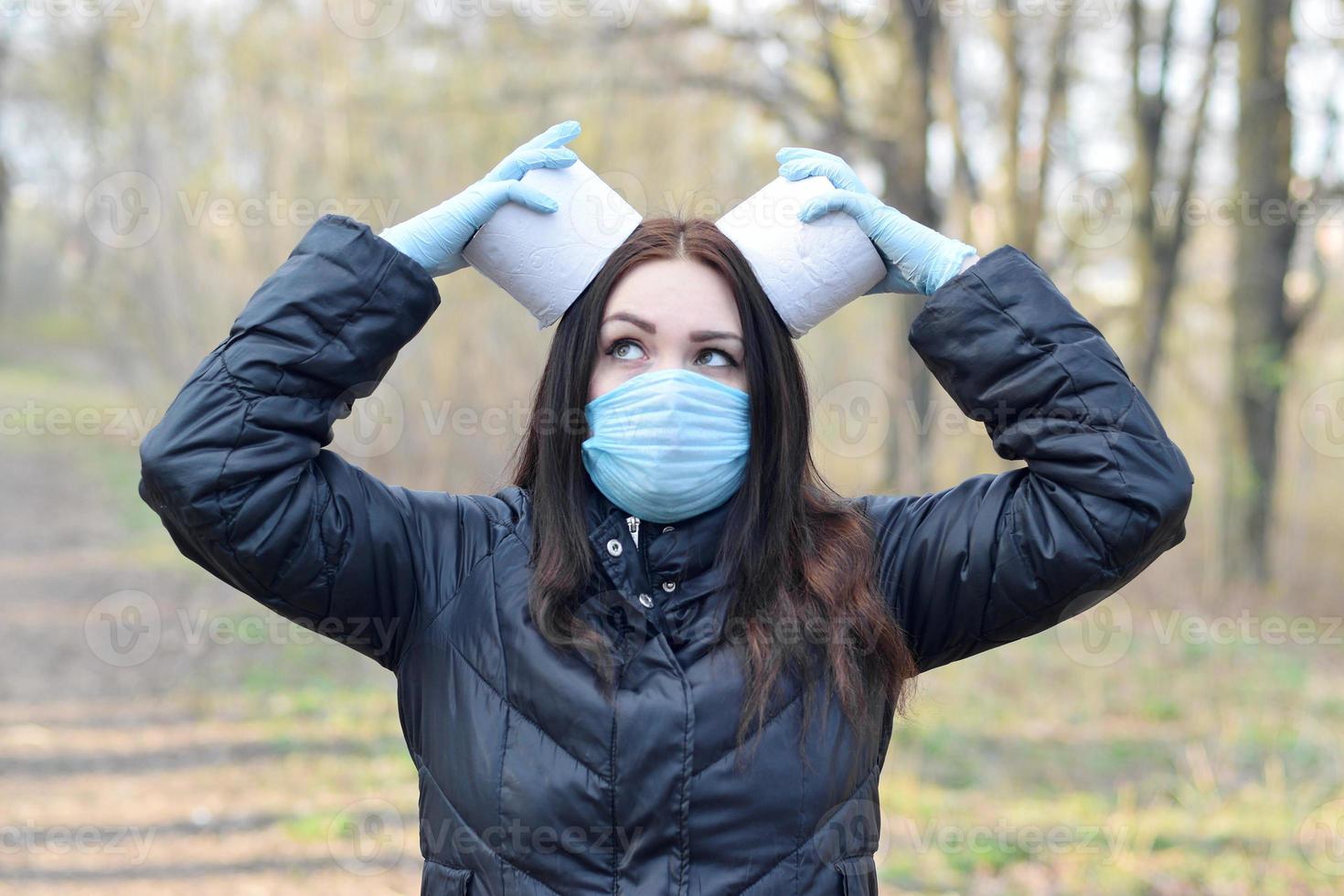 Covidiot concept. Young woman in protective mask holds many rolls of toilet paper outdoors in spring wood photo