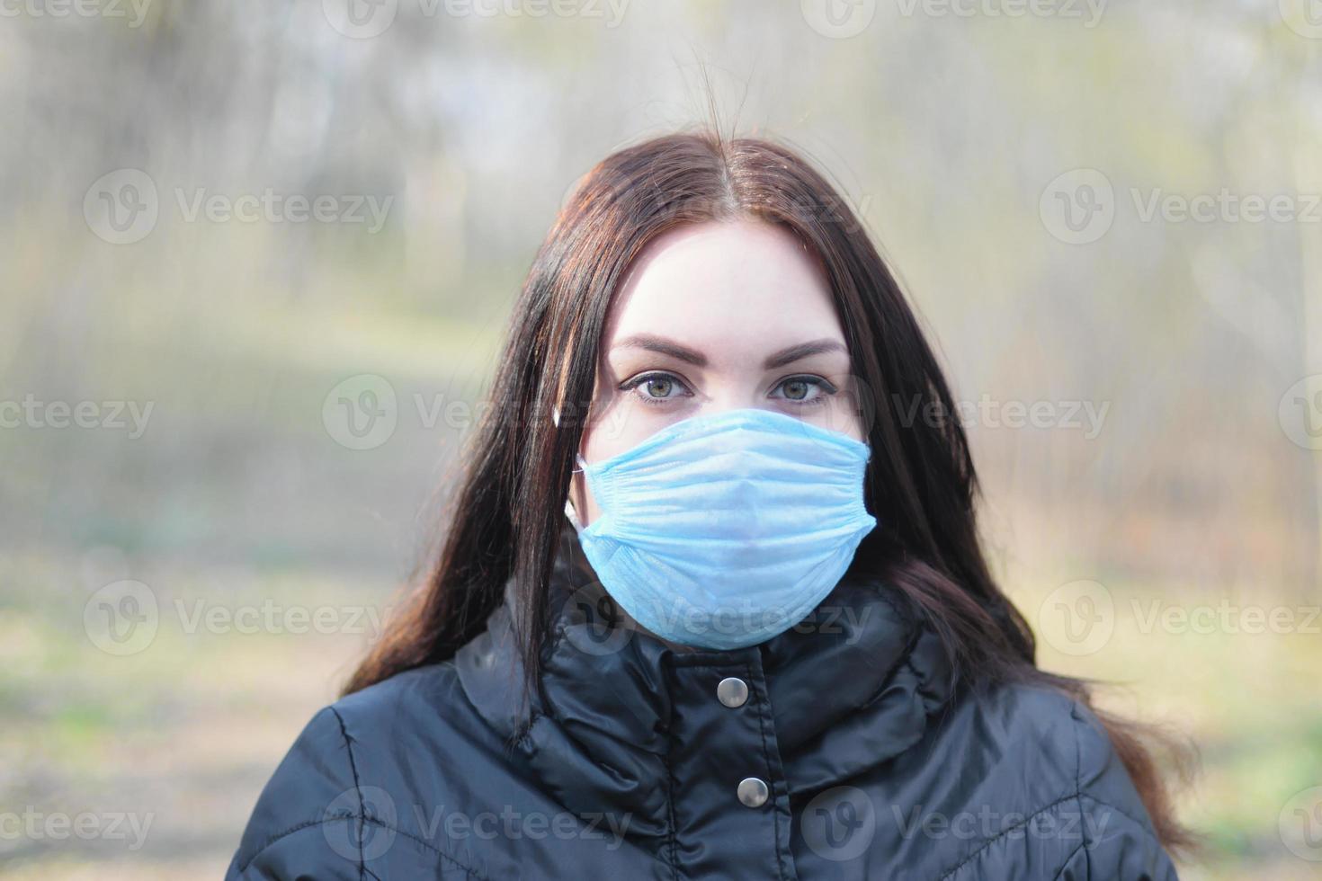 Portrait of young brunette woman in blue protective mask outdoors in spring wood photo