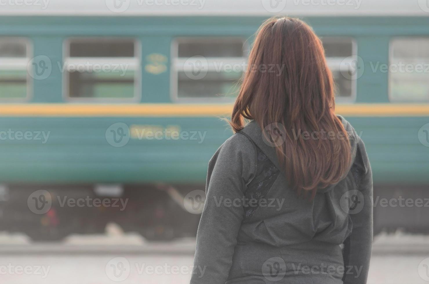 A young red-haired girl is standing on the railway platform and watching the departing train. The woman was late for her train. Back view photo