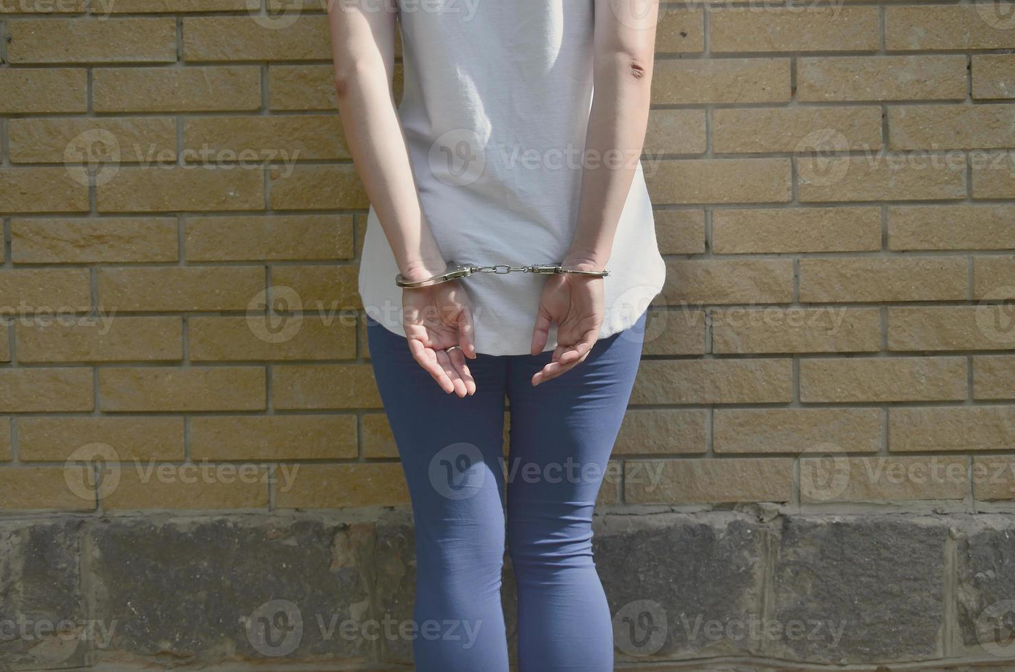 Fragment of a young criminal girl's body with hands in handcuffs against a yellow brick wall background. The concept of detaining an offender of a female criminal in an urban environment photo