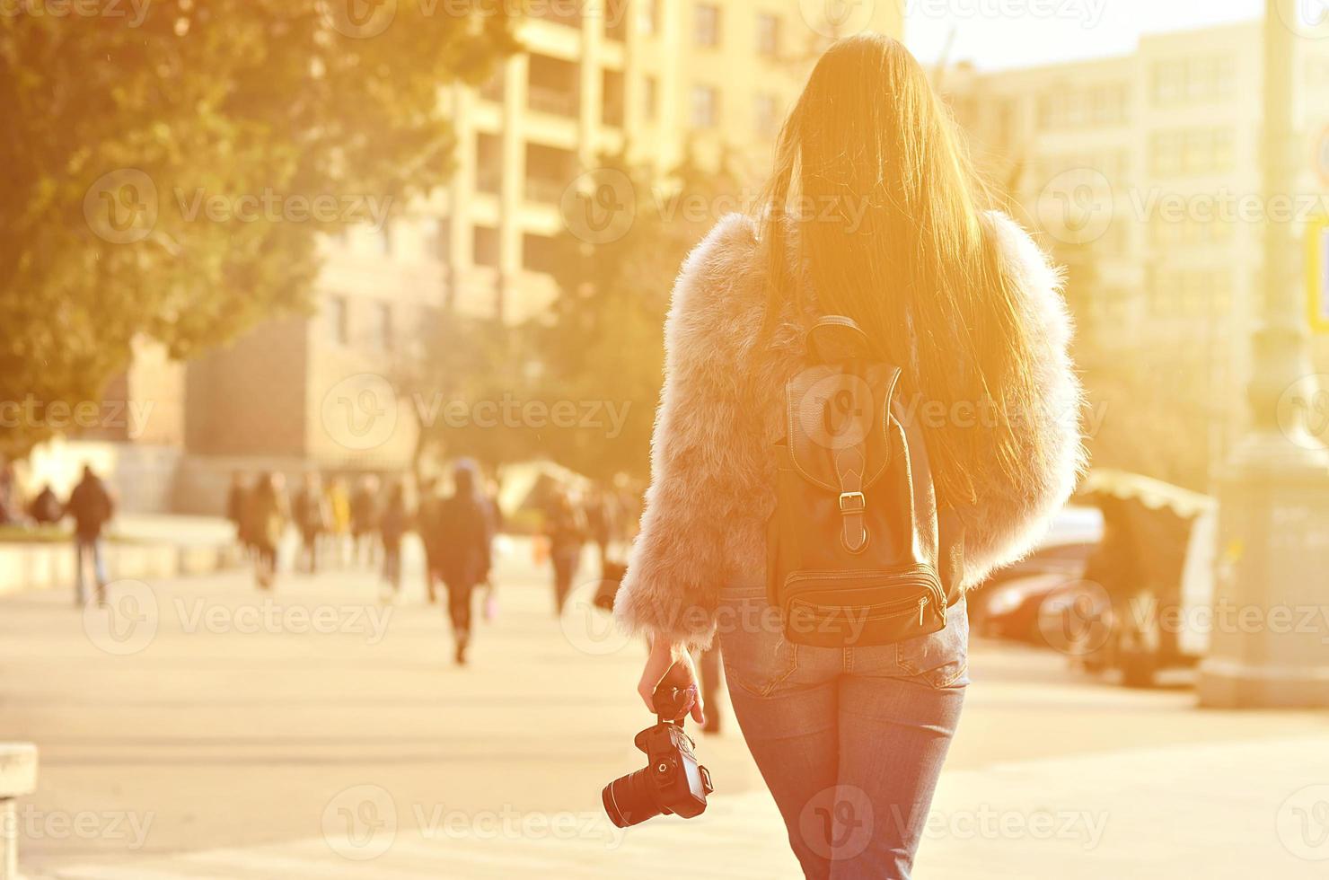 Rear view of a girl with a digital camera on a crowded street ba photo