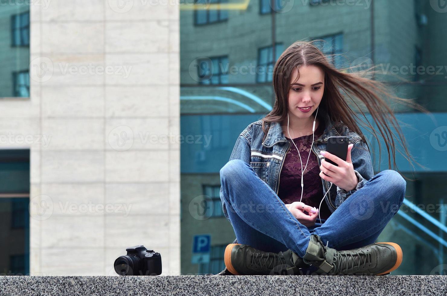 A girl photographer uses a smartphone and sits on a granite para photo