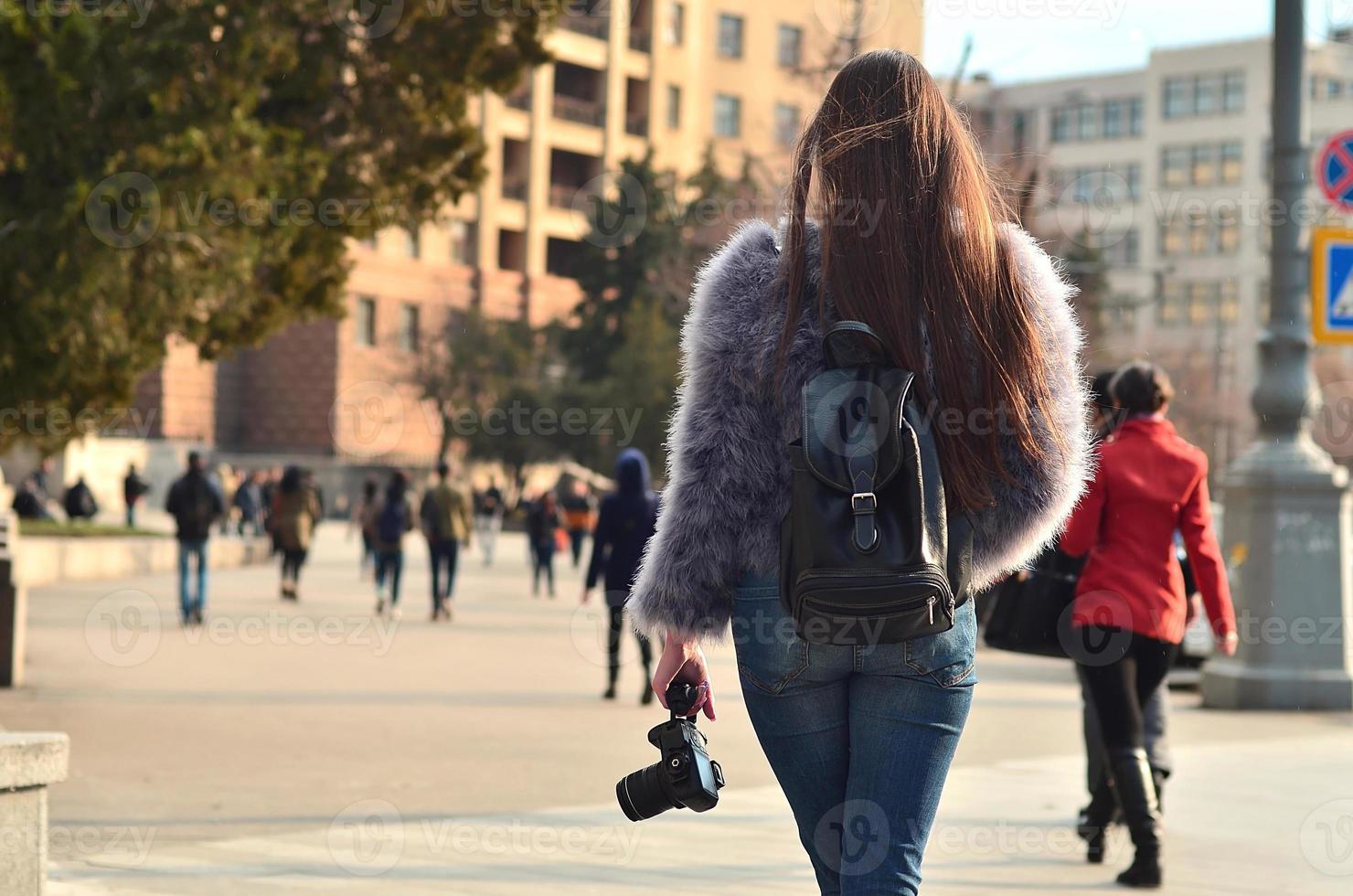 Rear view of a girl with a digital camera on a crowded street ba photo