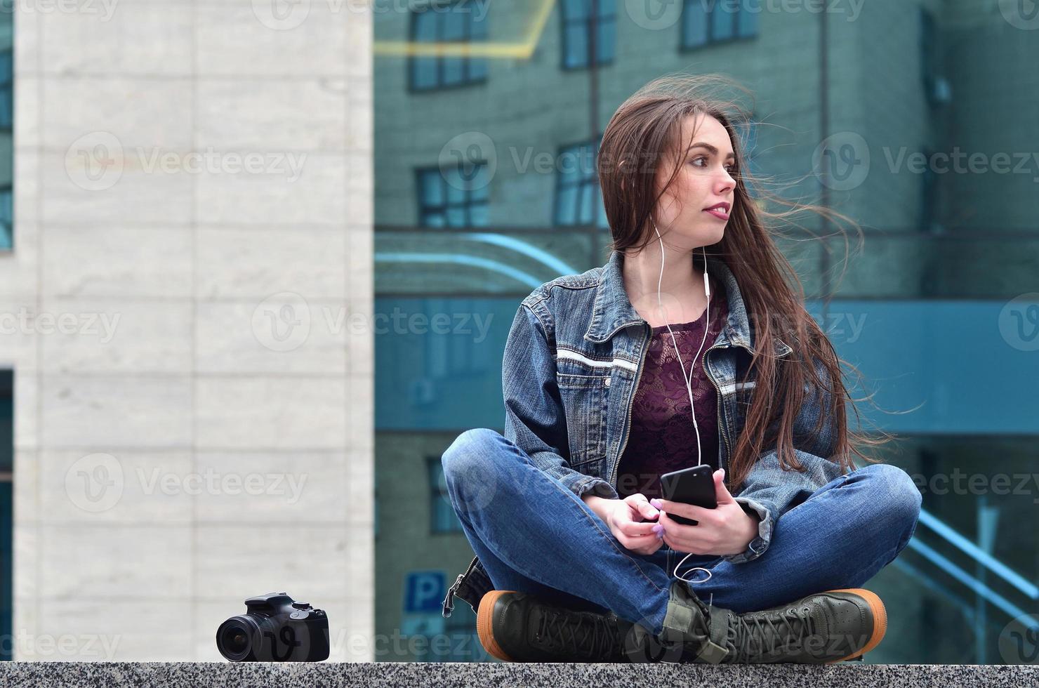 A girl photographer uses a smartphone and sits on a granite para photo