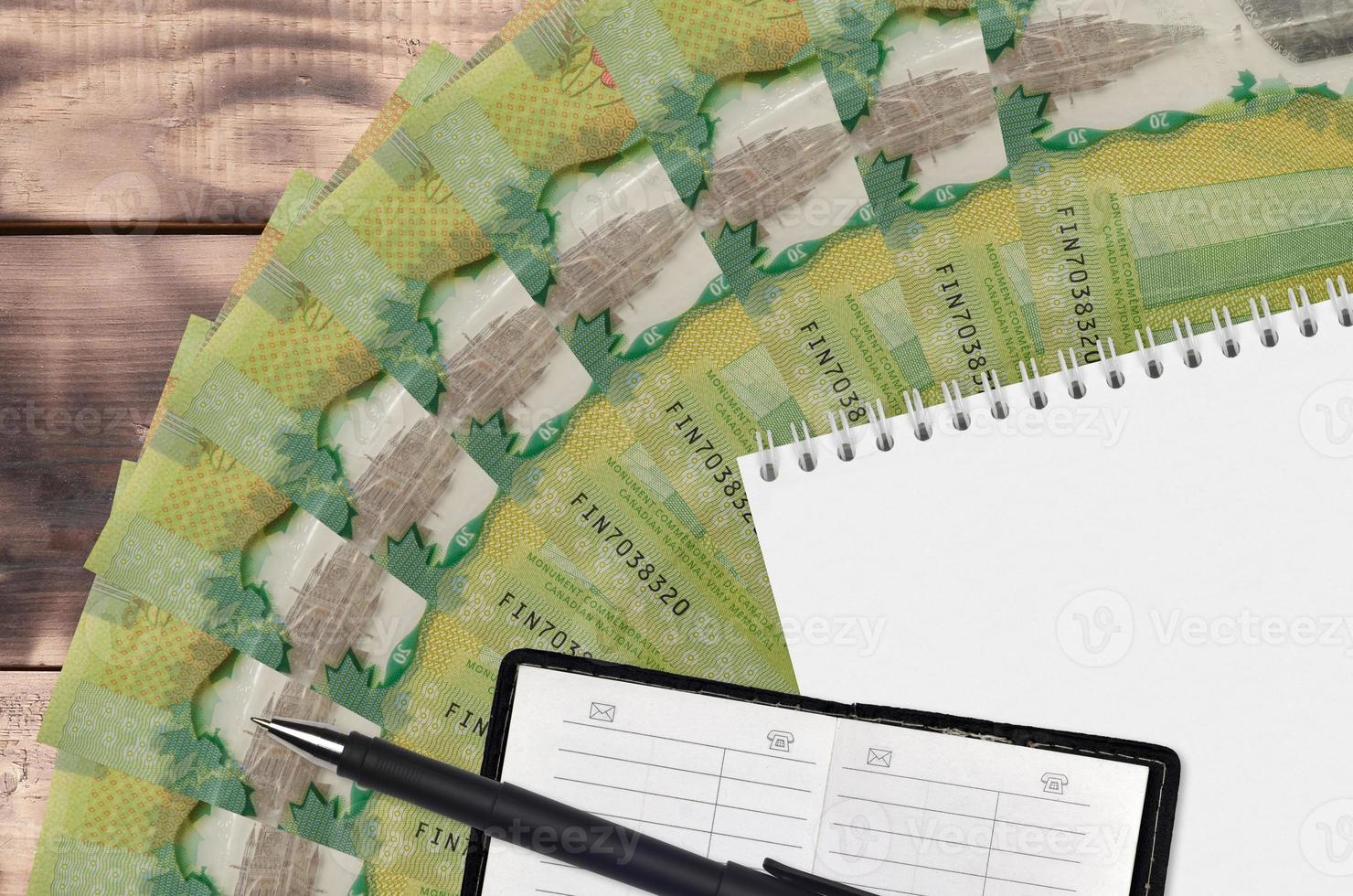 20 Canadian dollars bills fan and notepad with contact book and black pen. Concept of financial planning and business strategy photo