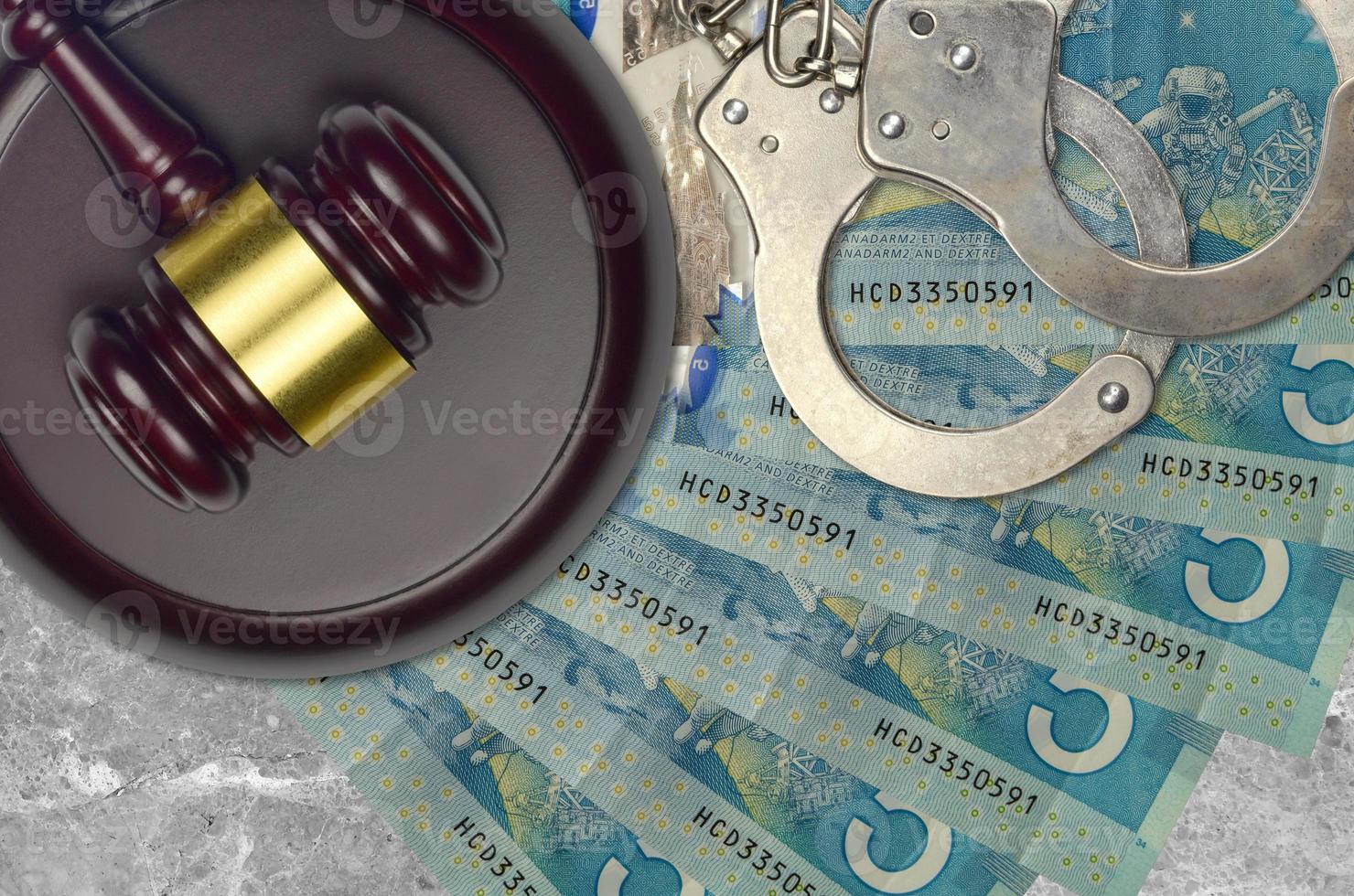 5 Canadian dollars bills and judge hammer with police handcuffs on court desk. Concept of judicial trial or bribery. Tax avoidance photo