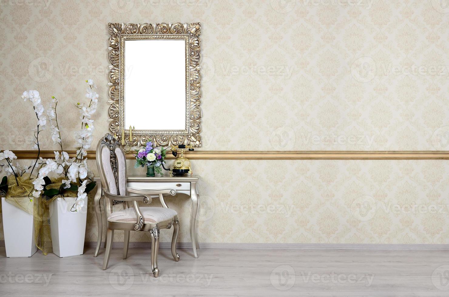 A fragment of a retro interior with a chair and table, on which is a telephone and a vase of flowers. Above the table hangs an empty picture frame for your photo