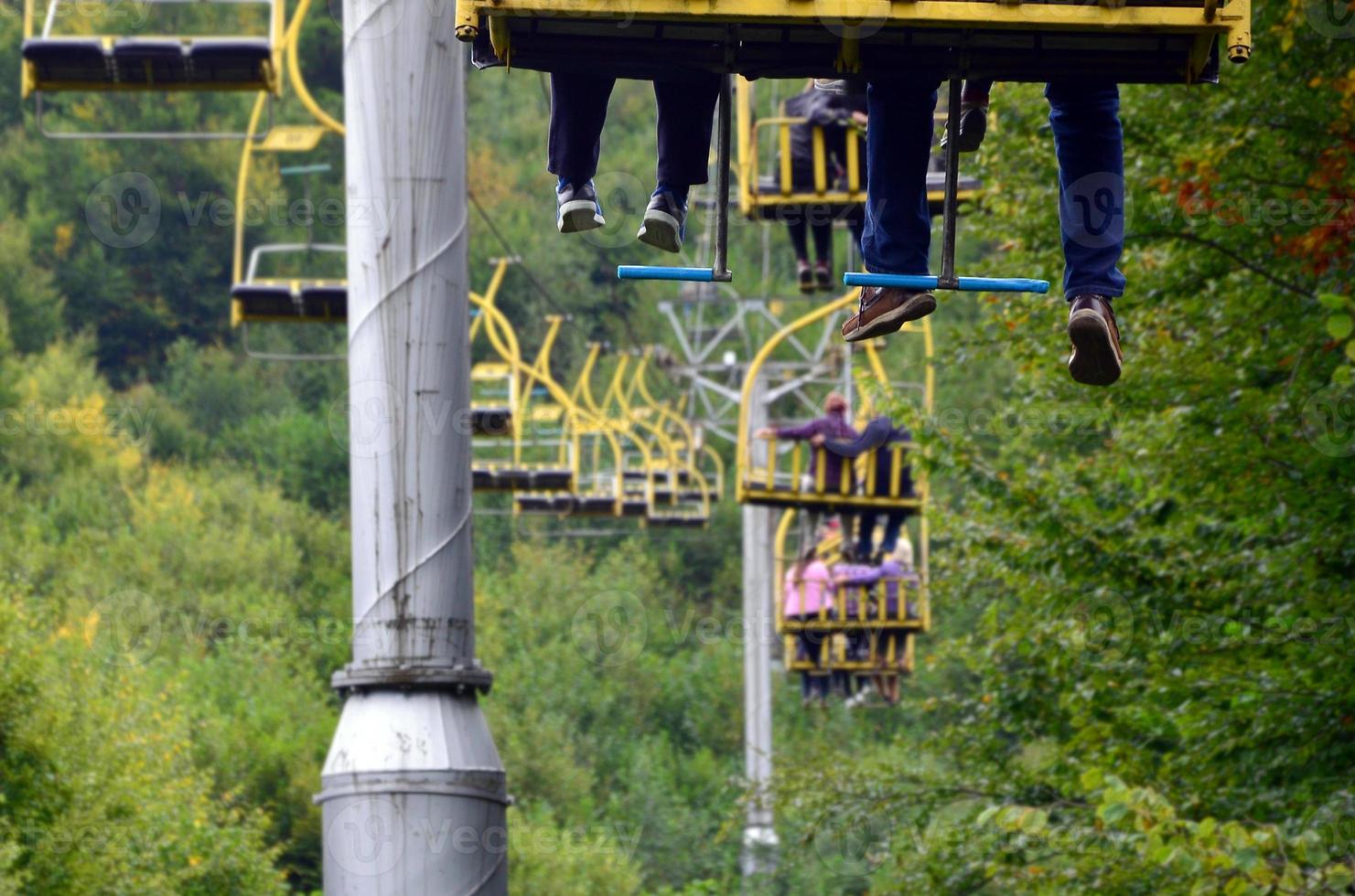 People ride on a cable car. The legs of passengers hang over the mountain forest photo