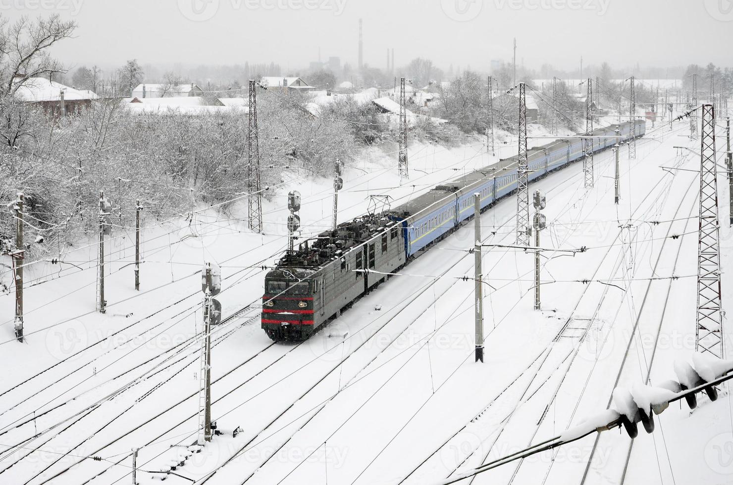 A long train of passenger cars is moving along the railway track. Railway landscape in winter after snowfall photo