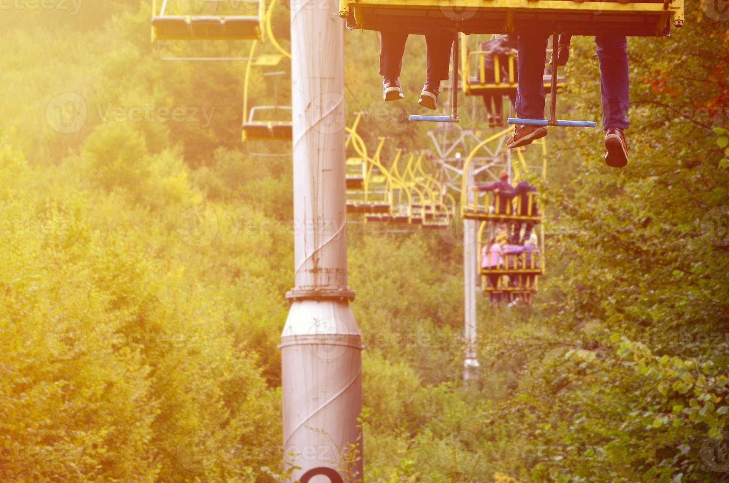 People ride on a cable car. The legs of passengers hang over the mountain forest photo