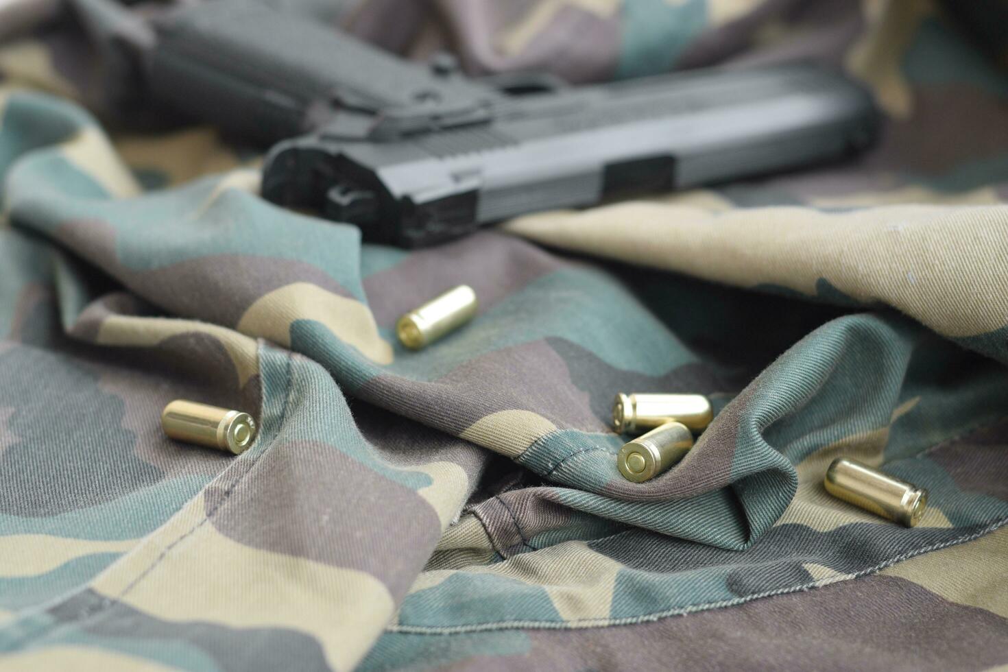Las balas de 9 mm y la pistola yacen sobre tela verde de camuflaje doblada. un conjunto de artículos de campo de tiro o un kit de defensa personal foto