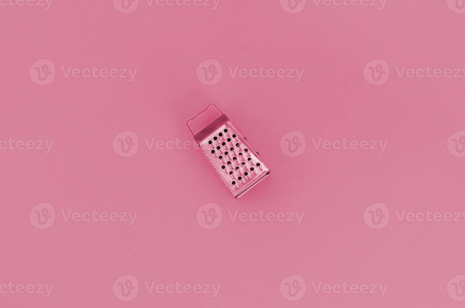 Stainless steel grater lies on a paper. Kitchen accessories. Tools for cooking. Image toned in Viva Magenta, color of the 2023 year photo