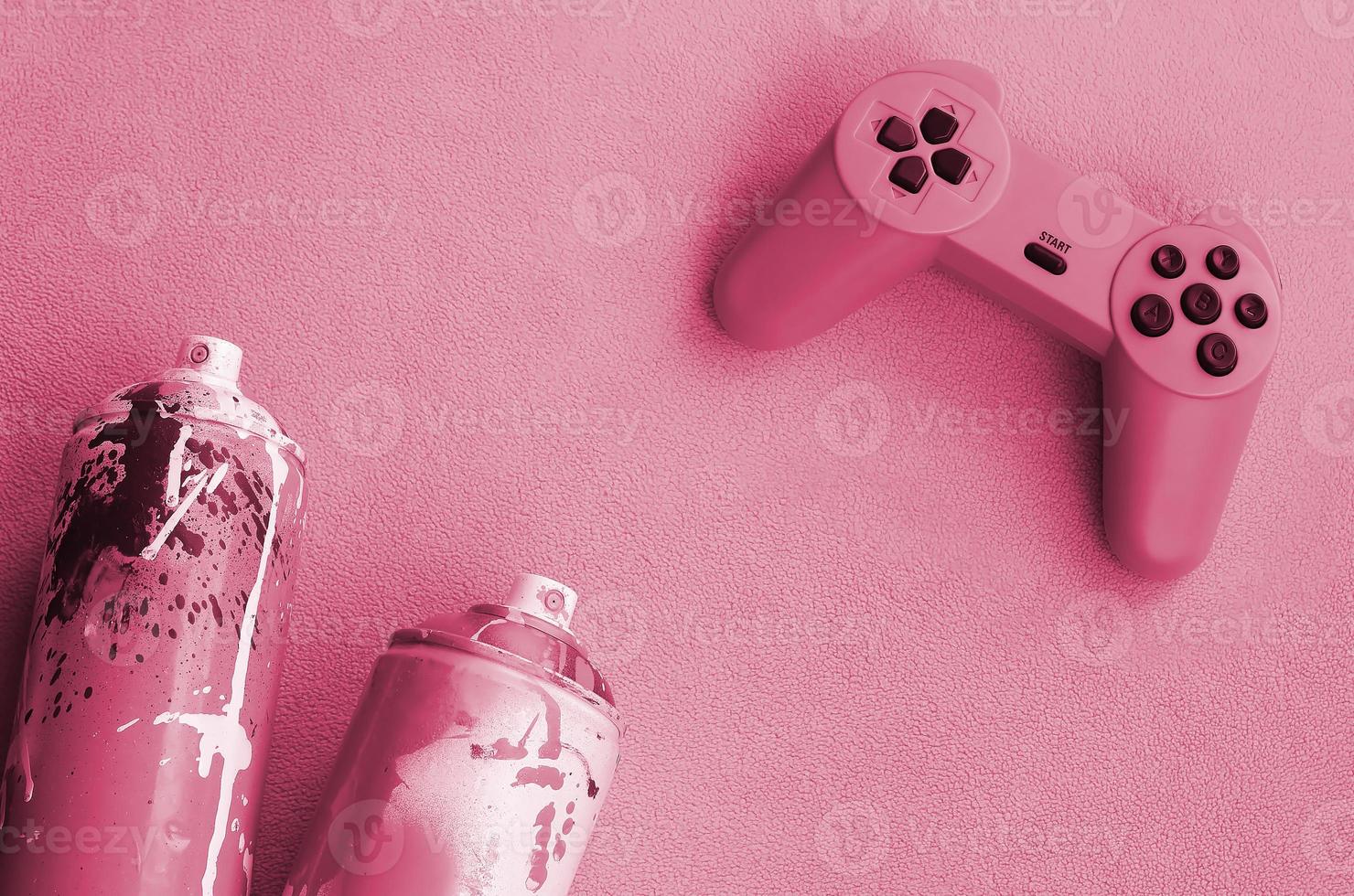 Teenagers and youth lifestyle concept. Joystick and two spray cans lies on the blanket Image toned in Viva Magenta, color of the 2023 year photo