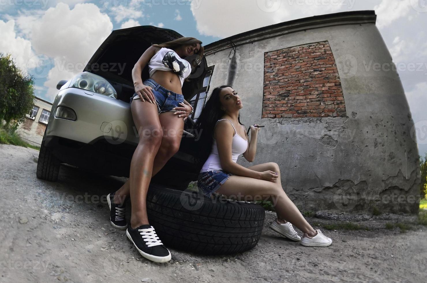 Two young and sexy girls with wheel wrenches around a silvery ca photo