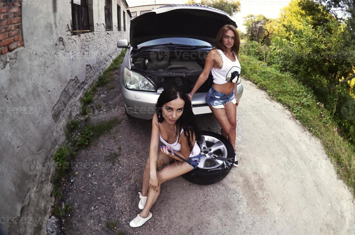 Two young and sexy girls with wheel wrenches around a silvery ca photo