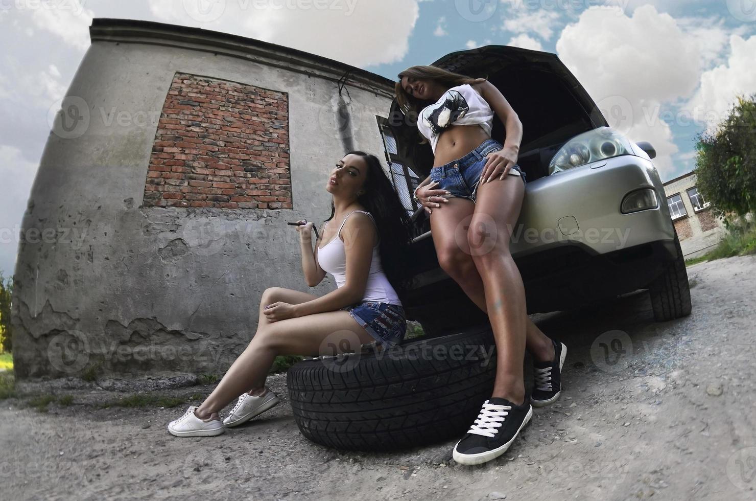 Two young and sexy girls with wheel wrenches around a silvery ca photo