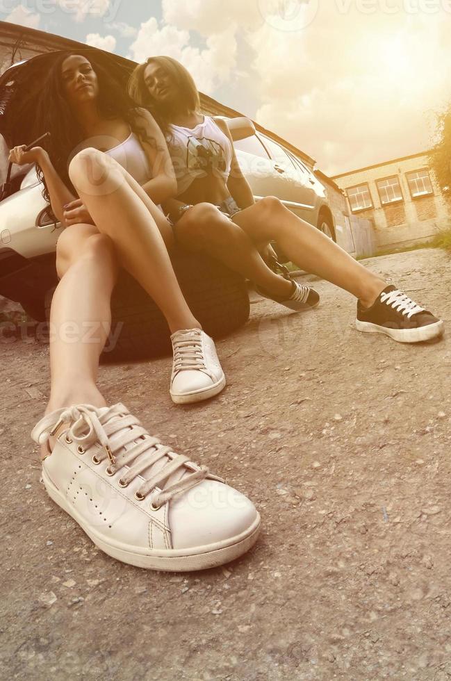 Two young and sexy girls with wheel wrenches around a silvery ca photo