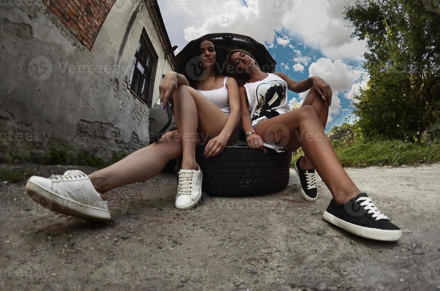 Two young and sexy girls with wheel wrenches around a silvery ca photo