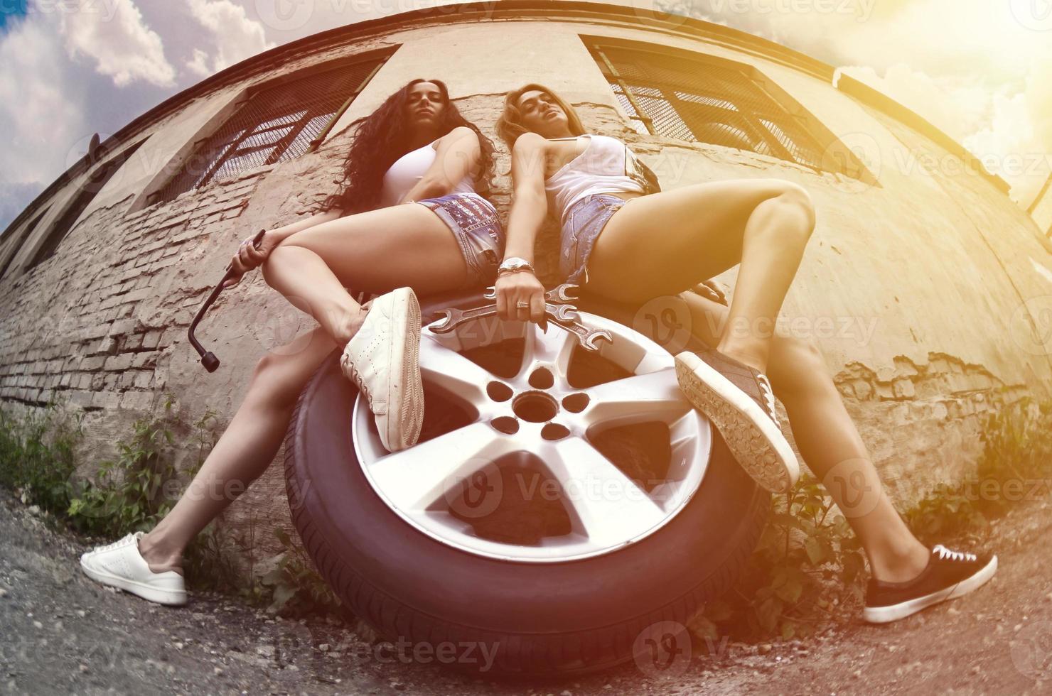 Two young and sexy girls with wrenches are sitting on the car wh photo