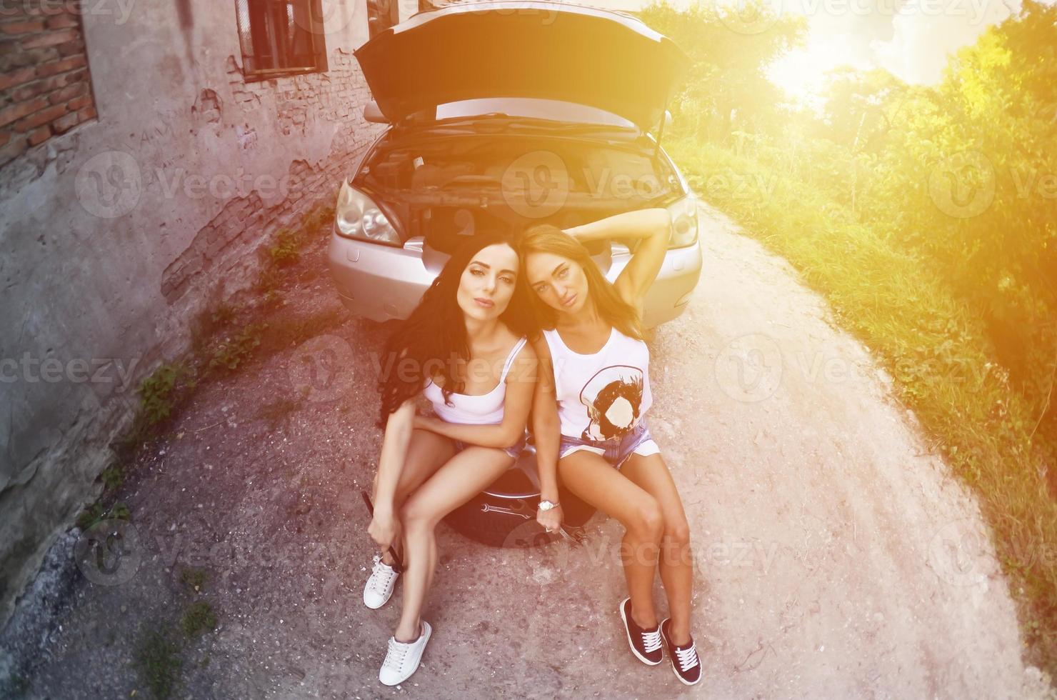Two young and sexy girls with wheel wrenches around a silvery ca photo
